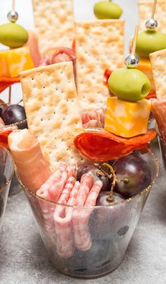 an assortment of crackers, olives, and cheese sticks are arranged in small cups