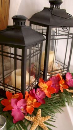 two black lanterns sitting next to each other on top of a table with flowers in front of them