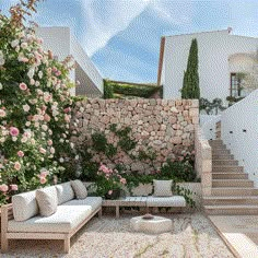 an outdoor seating area in front of a stone wall with flowers and greenery on it