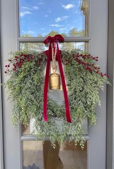 a christmas wreath hanging from the front door with a bell on it's side