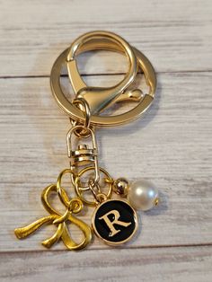 a gold keychain with an initial and ribbon on it, sitting on a wooden surface