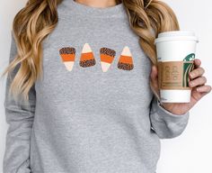 This cozy candycorn sweatshirt is the perfect addition to any fall wardrobe this season. Featuring a cute patterned design of 4 candycorn, with an added touch of leopard print, pairs well with leggings or jeans. Spend over 35 and get free shipping! Ideal for any situation, a unisex heavy blend crewneck sweatshirt is pure comfort. These garments are made from polyester and cotton. This combination helps designs come out looking fresh and beautiful. The collar is ribbed knit, so it retains its shape even after washing. There are no itchy side seams on these sweaters.  .: 50% cotton, 50% polyester .: Medium-heavy fabric (8.0 oz/yd² (271.25 g/m .: Loose fit .: Sewn-in label .: Runs true to size ---ABOUT THIS UNISEX SWEATSHIRT--- ♥ BRAND: GILDAN (18000) ♥ 9 COLORS ♥ 8 SIZES - SIZE CHART AVAILAB Candy Corn Outfit, Candy Corn Sweater, Candy Corn Necklace, Halloween Cotton Sweatshirt With Graphic Print, Corn Shirt, Candy Corn Shirt, Halloween Cotton Pre-shrunk Sweatshirt, Fall Candy, Halloween Crewneck