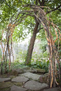 an arch made out of sticks and branches in the middle of a stone path surrounded by trees