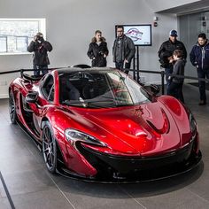 people standing around a red sports car in a showroom with others looking at it