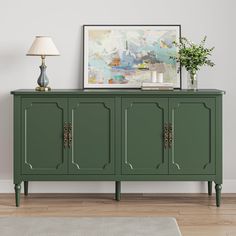 a green sideboard with three doors and two lamps on it in front of a white wall