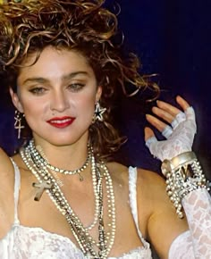 a woman with curly hair wearing white gloves and pearls on her head, holding two bracelets