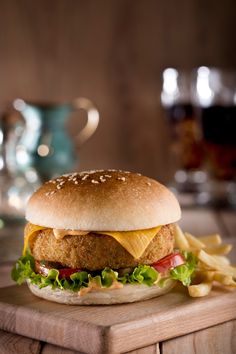 a chicken sandwich with lettuce, tomato and cheese on a wooden cutting board