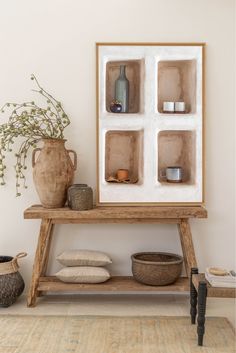 a wooden table topped with lots of vases next to a wall mounted art piece