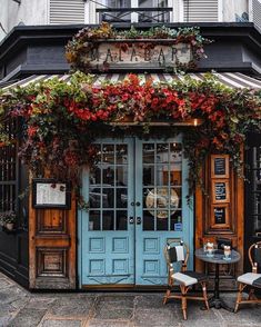 two tables and chairs in front of a blue door with flowers on it's side