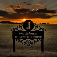 a sign that is in the middle of a field with a sun setting behind it