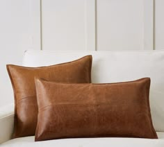 two brown leather pillows sitting on top of a white couch