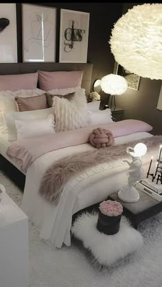 a white bed with pink and grey pillows on top of it in a bedroom next to two lamps