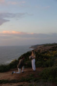 two people standing on top of a hill next to the ocean