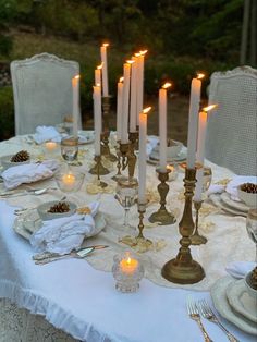 a table topped with lots of white plates and glasses filled with lit candles next to each other