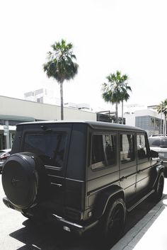 a black mercedes benz is parked on the side of the road with palm trees in the background