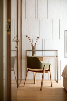 a chair sitting in front of a table with a vase on top of it next to a bed