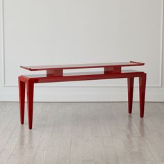 a red table sitting on top of a hard wood floor next to a white wall