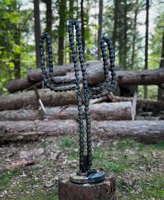 a chain - wrapped cactus sculpture stands in the middle of a forest, surrounded by logs