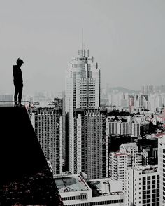 a man standing on top of a tall building with a city in the back ground