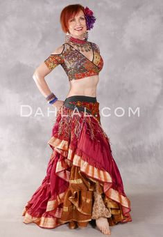 a woman with red hair wearing a belly dance outfit and matching headpiece, standing in front of a gray background