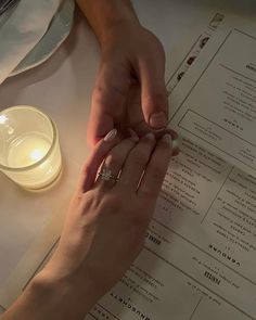 two people holding hands on top of a table next to a candle and menus