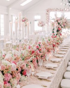 a long table is set with white plates and pink flowers, candles and centerpieces