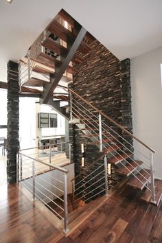 a stair case in the middle of a room with wood floors and stone wall behind it