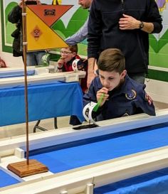 a young boy in uniform is looking at something on the table while an adult watches