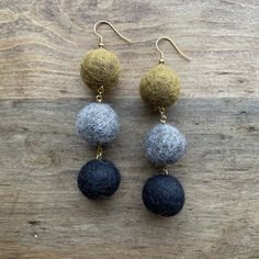 three different colored balls hanging from gold and silver earwires on a wooden surface