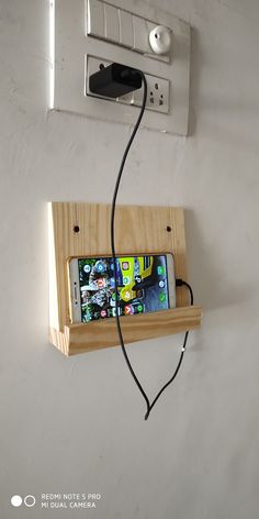 a cell phone is plugged into a wooden holder on the wall with wires attached to it