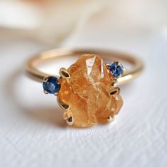 a gold ring with two blue sapphire stones on the front and center, sitting on a white surface