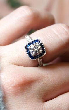 a woman's hand holding a ring with a blue and white diamond in it