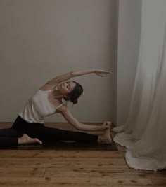 a woman is doing yoga in front of a white curtain with her arms stretched out