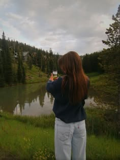 a woman standing in front of a lake taking a photo