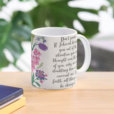 a coffee mug sitting on top of a wooden table next to a book and plant