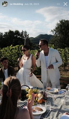 a man and woman standing in front of a table with food on it, surrounded by other people