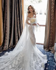 a woman in a wedding dress standing by a window