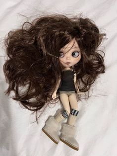 a doll with long brown hair laying on top of a white sheet