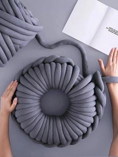 two hands are reaching for an object that looks like a spiral pillow with a book on it