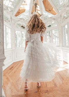 a woman in a white dress standing on a wooden floor with her back to the camera