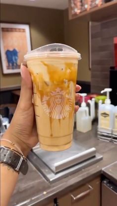 a person holding up a starbucks drink in front of a counter with other drinks on it