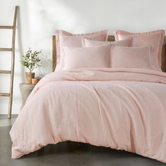 a bed with pink linens and pillows in a white room next to a ladder