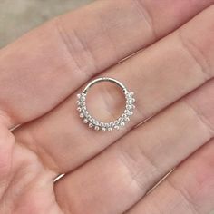 a woman's hand holding a small silver ring with white stones on it,