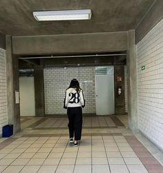 a woman walking down a hallway in an empty building with white tiles on the floor