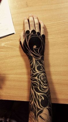 a person's arm with tattoos on it sitting at a desk next to a pen and paper