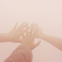 four hands reaching up into the air to reach something in the sky with fog on it