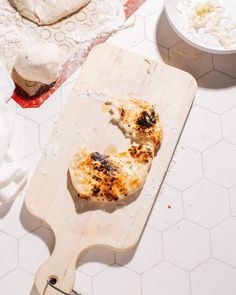 a wooden cutting board topped with food on top of a white tiled counter next to bowls and utensils