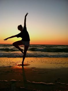 a woman standing on top of a sandy beach next to the ocean at sun set