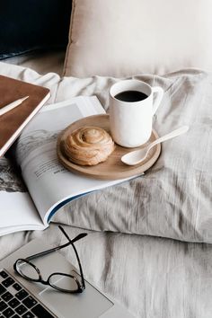 a cup of coffee and some kind of pastry on a bed with a laptop computer