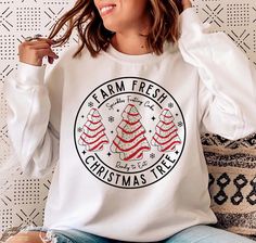 a woman wearing a farm fresh christmas tree t - shirt sitting on a couch with her hands in her hair